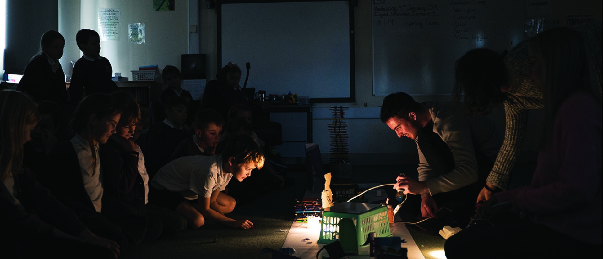 Teacher shows demonstrates a creative project on the floor to a group of children.