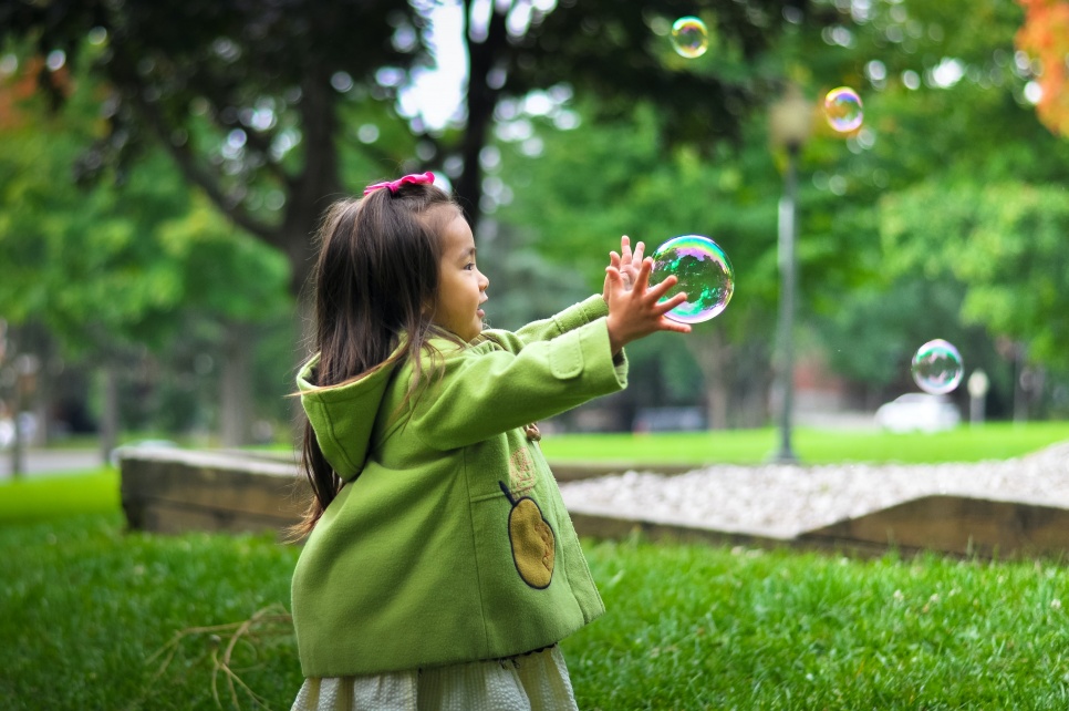 A child standing outdoors, catching a bubble
